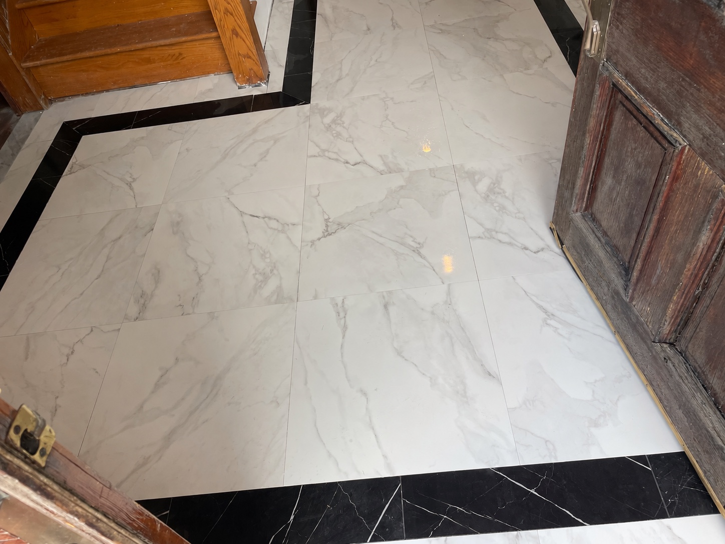 White marble-look entry floor with a black tile border and wooden doors