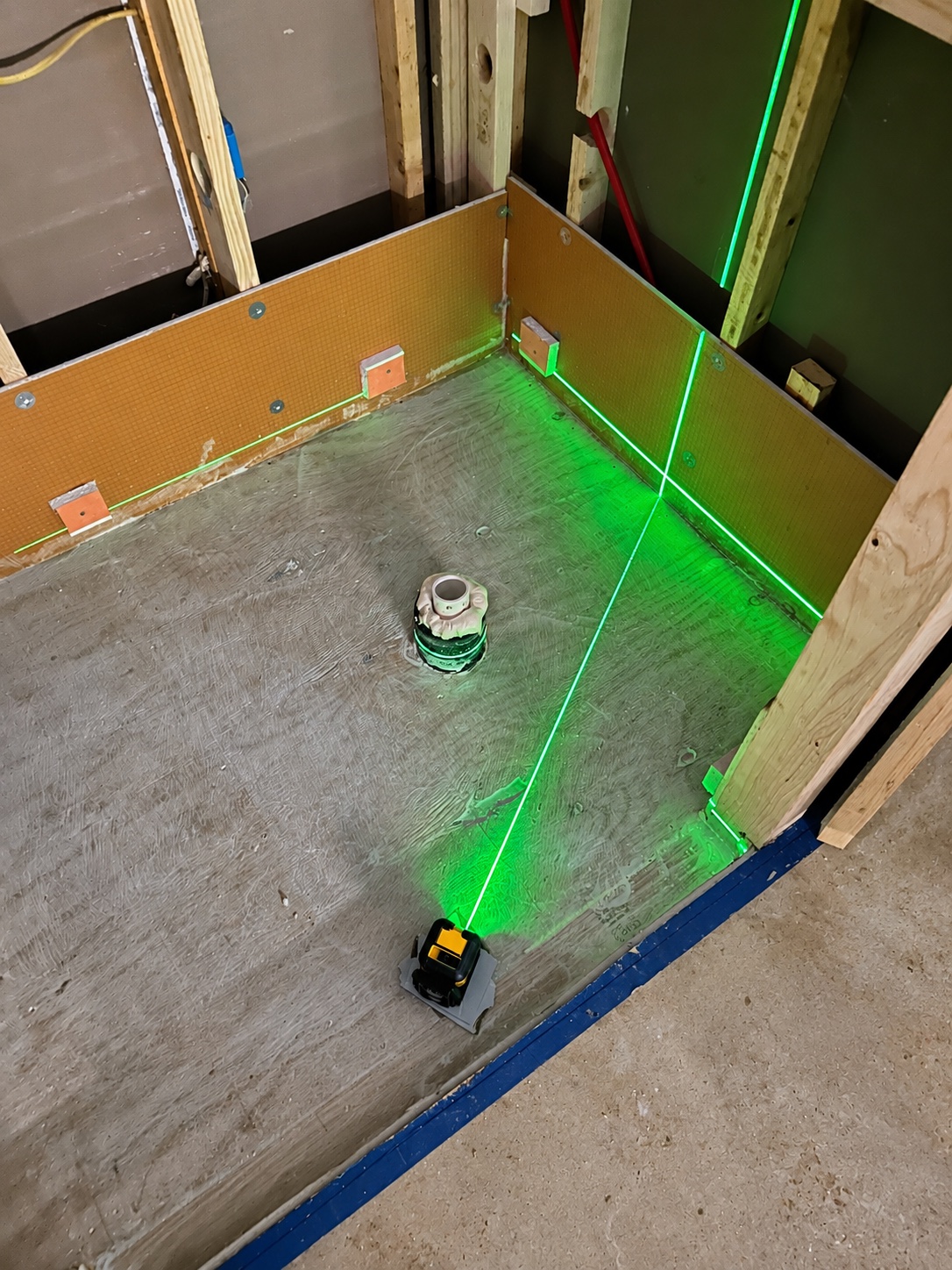 Laser layout check over a shower base with exposed wall framing during preparation