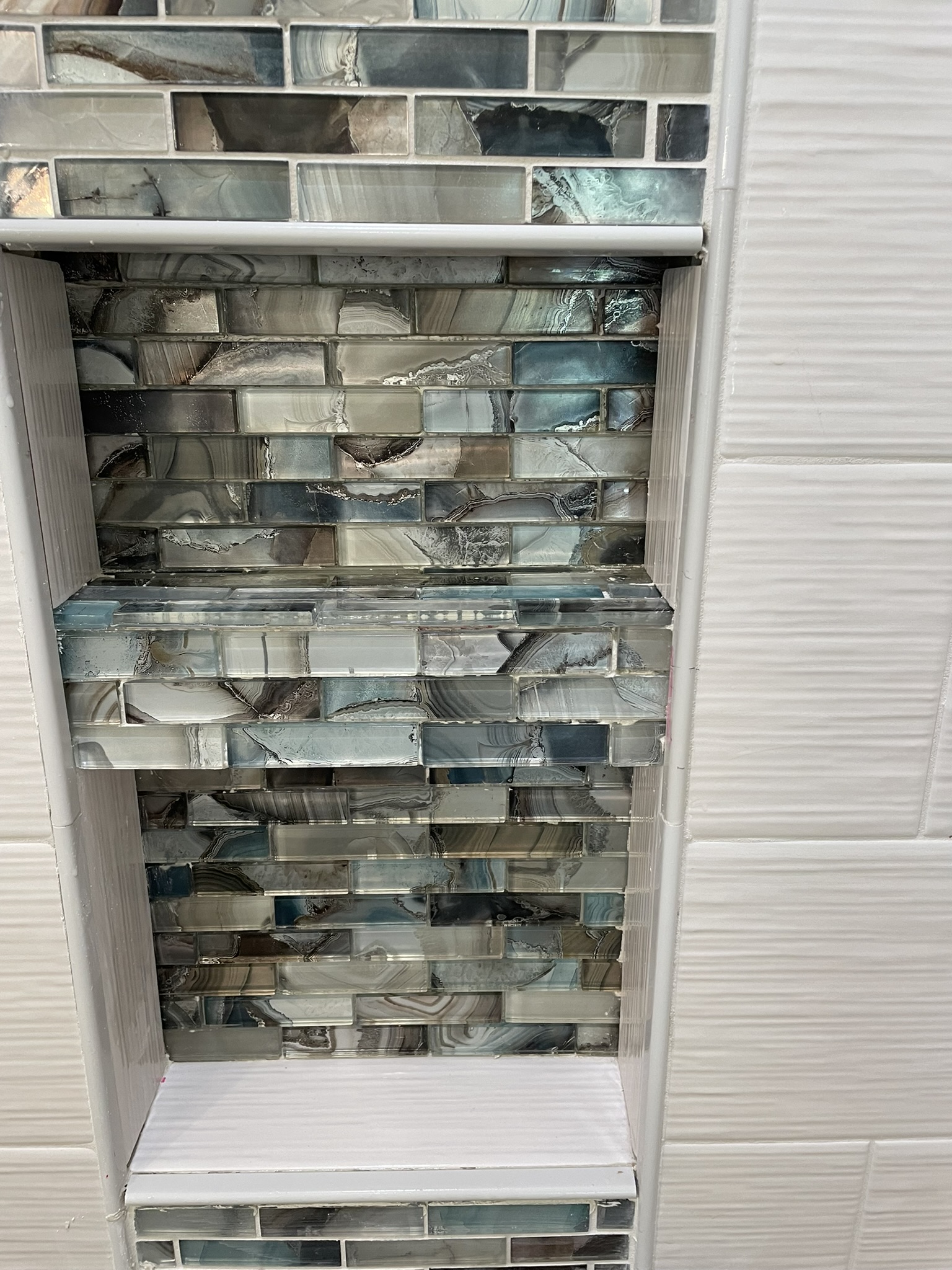 Glass mosaic shower niche framed with white tile trim